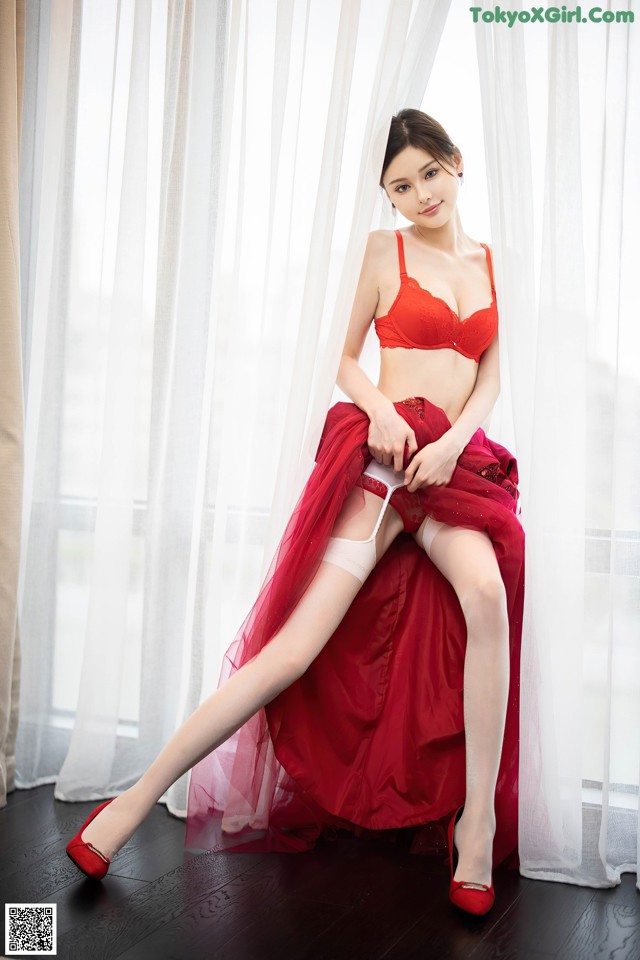 A woman in a red lingerie sitting on a window sill.