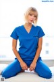 A woman in scrubs sitting on a bed in a hospital room.