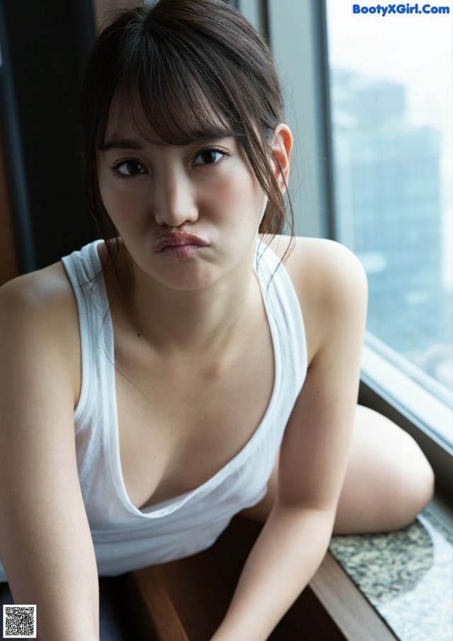 A woman in a white tank top sitting on a window sill.