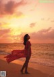 A woman in a red dress standing on the beach at sunset.