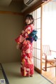 A woman in a red kimono standing in front of a window.