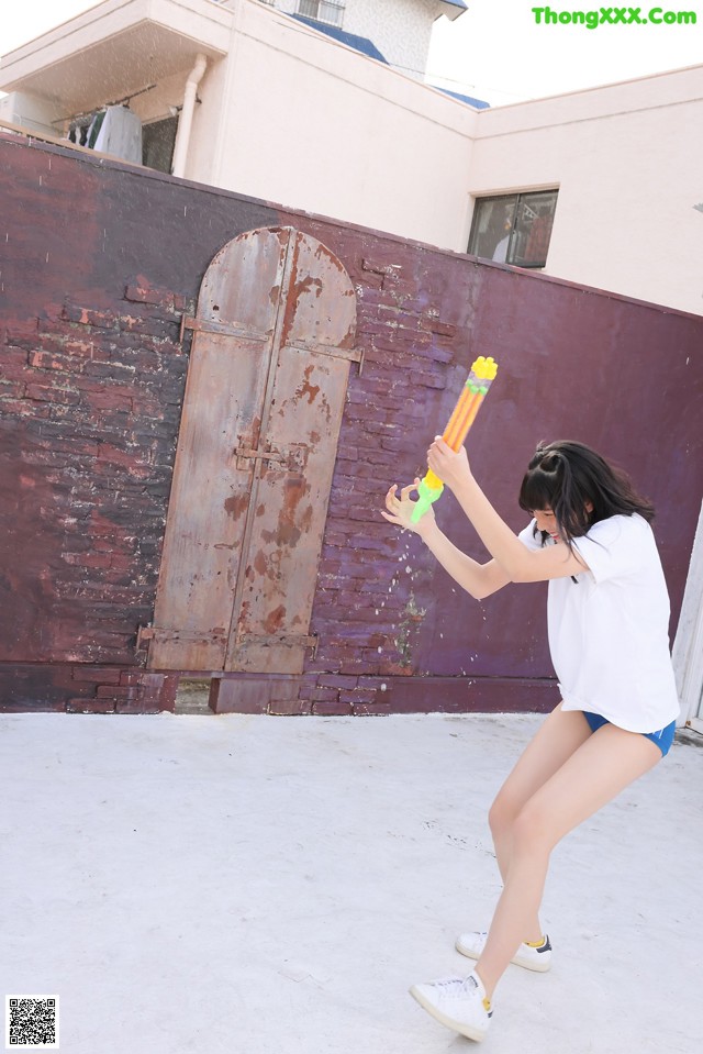 A woman in a white shirt and blue shorts holding a water gun.