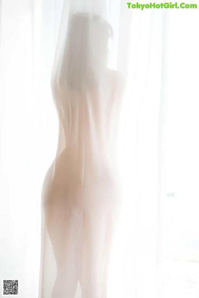 A nude woman standing in front of a white curtain.