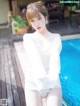 A woman in a white shirt is posing by a pool.