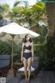 A woman in a black bikini standing under an umbrella.