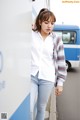 A woman leaning against a wall in front of a bus.